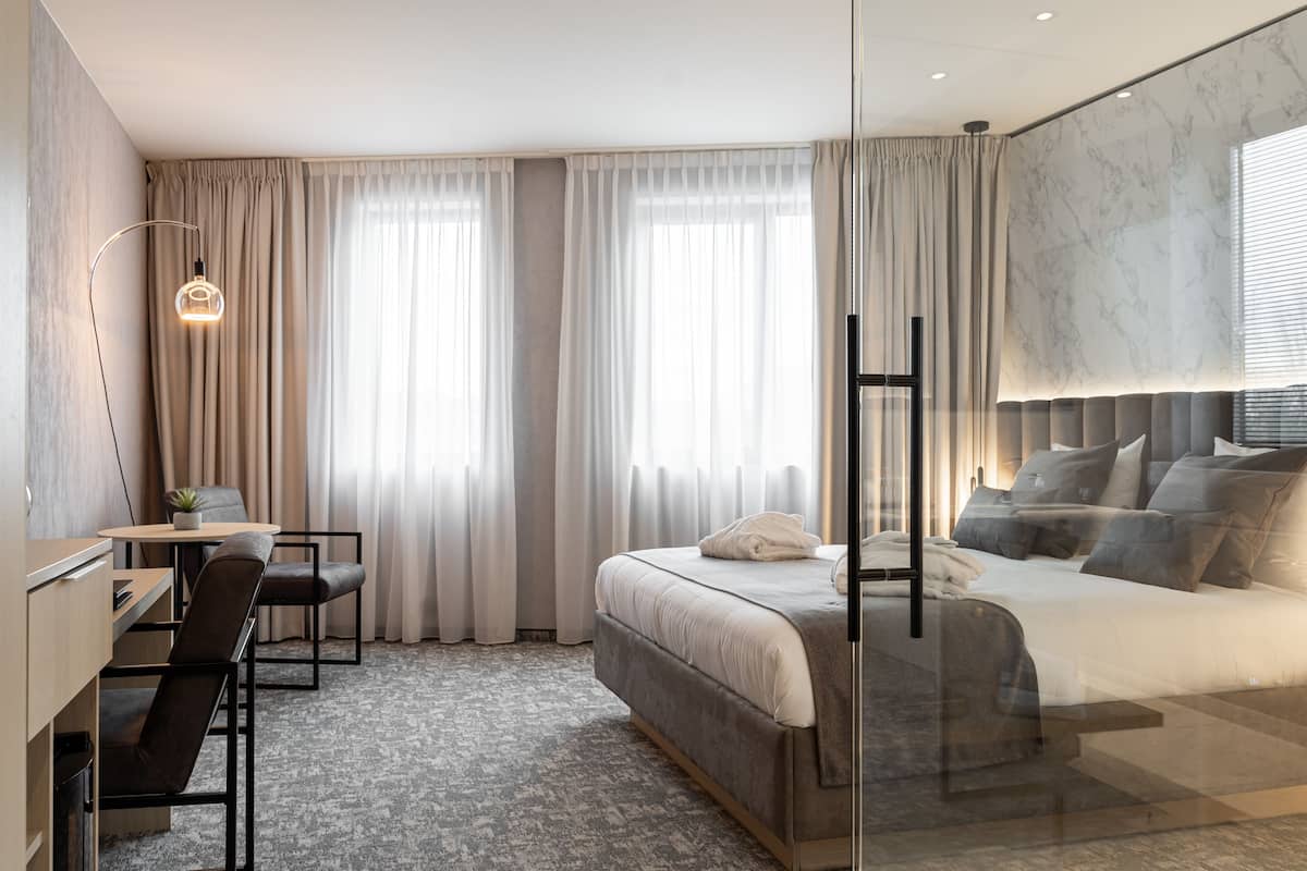 A modern hotel room with a bed, a desk, a chair, and a large window with curtains.