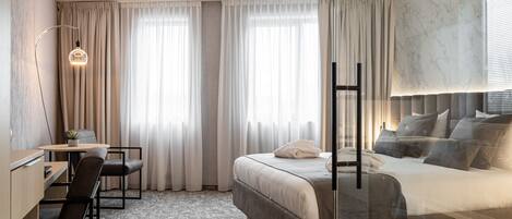 Una habitación de hotel moderna con cama, escritorio, silla y un ventanal con cortinas.