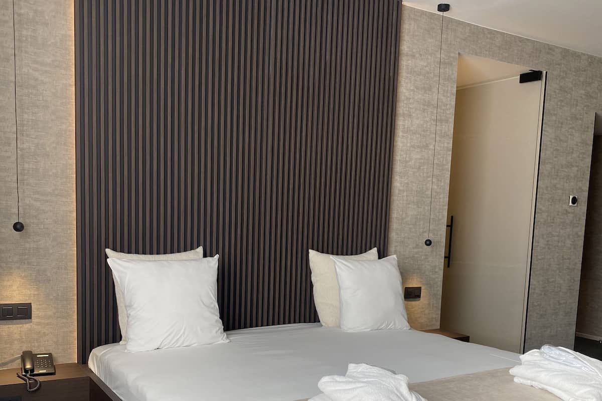 A modern hotel room with a large bed, two bedside tables, a bedside phone, and a mirror.