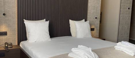 Una habitación de hotel moderna con una cama grande, dos mesitas de noche, un teléfono junto a la cama y un espejo.