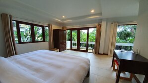 A hotel room with a large bed, a desk, and a balcony with a view of greenery. - NB Villa Celina (Koh Samui)