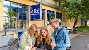 Three people standing outside a building with a blue sign reading "a&o hostels.com". - a&o Stuttgart City - Hostel (Stuttgart)