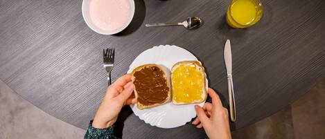A table with a plate of toast, a bowl of yogurt, an apple, a glass of juice, a spoon, a fork, and a knife.