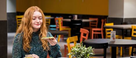 Una persona sentada a una mesa con comida, un vaso de zumo de naranja, una manzana verde y una planta en maceta.