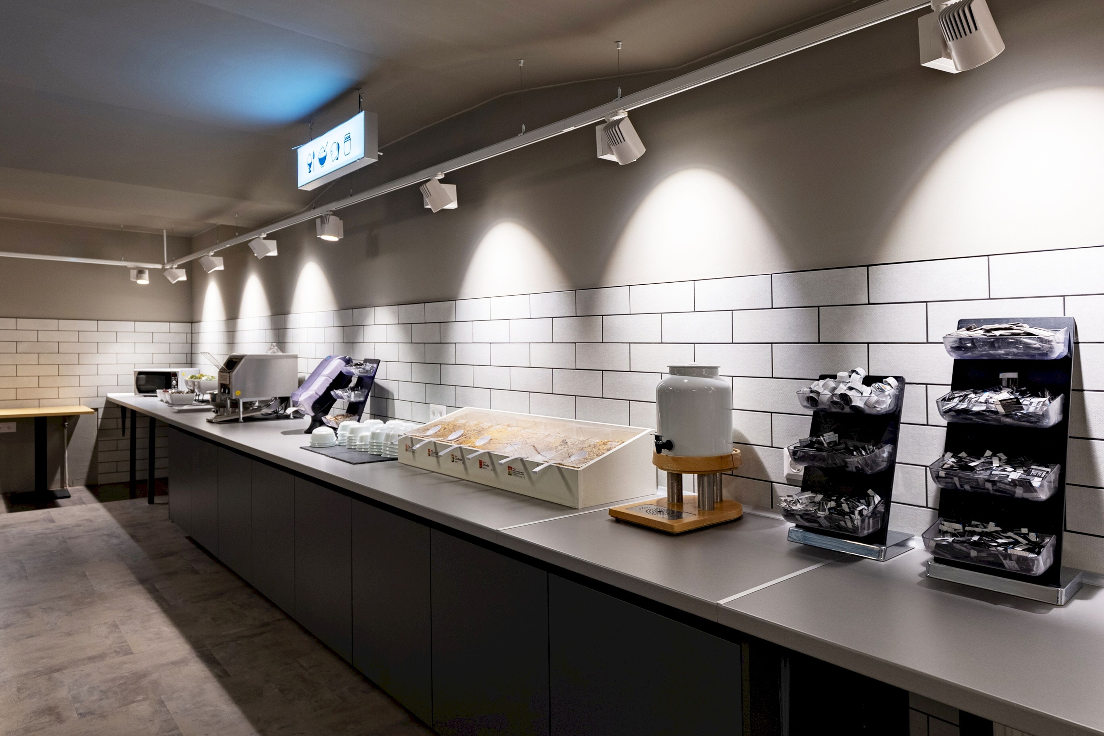 A modern kitchen with a long counter, equipped with a coffee machine, a kettle, and a food display.