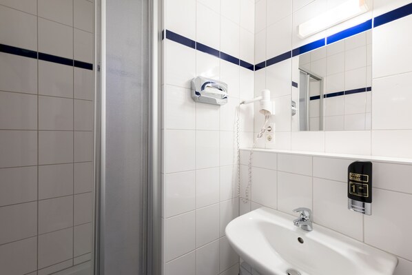 Une salle de bain avec des carreaux blancs, un sèche-mains, un lavabo et un miroir.
