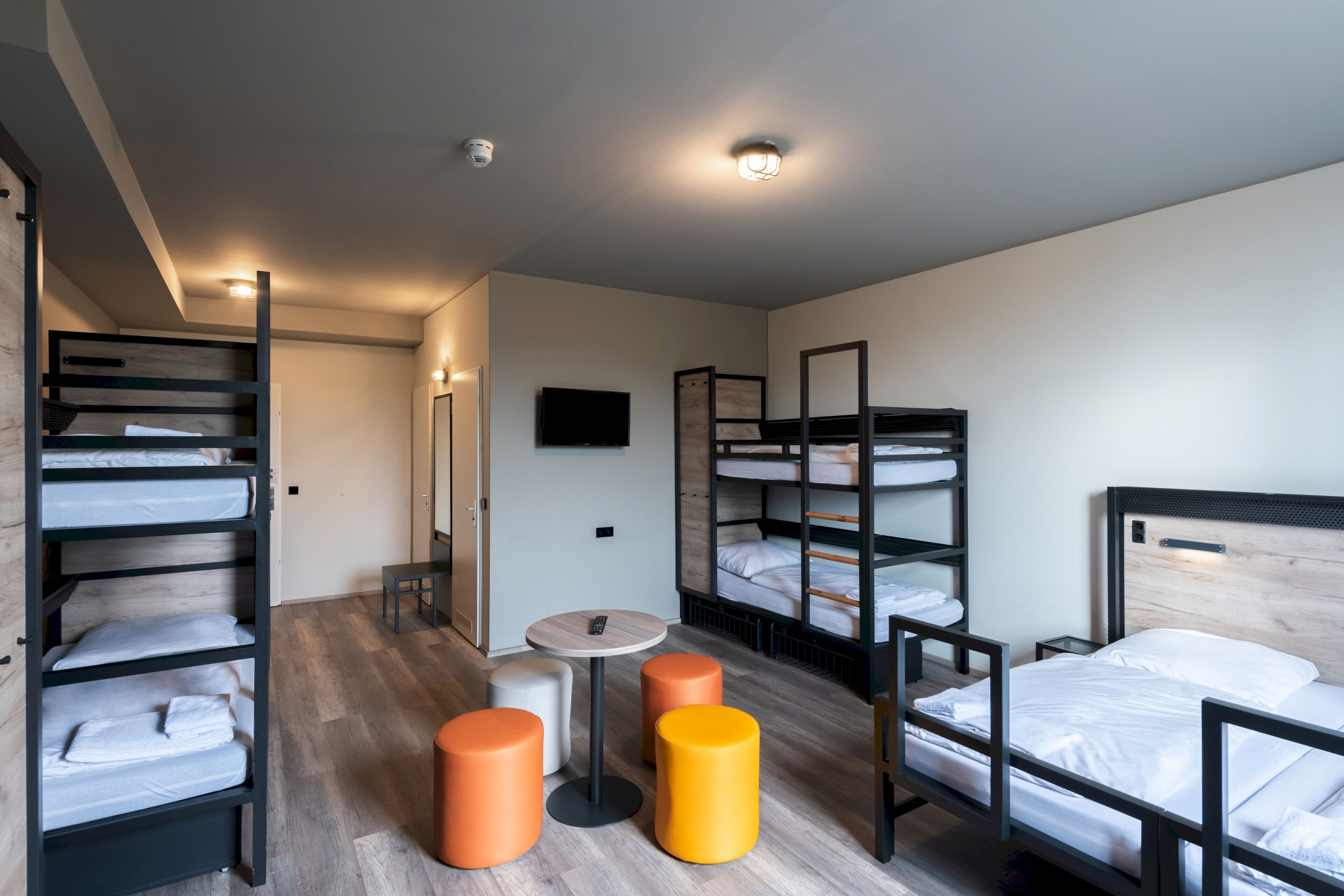 A modern hotel room with bunk beds, a small round table, and two stools.