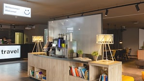 A reception desk with a modern design, a digital screen displaying a welcome message, and a bookshelf filled with books. - a&o Stuttgart City - Hostel (Stuttgart)