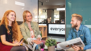 Three people seated at a table in a modern indoor setting with a large 'everyone' sign in the background. - a&o Stuttgart City - Hostel (Stuttgart)