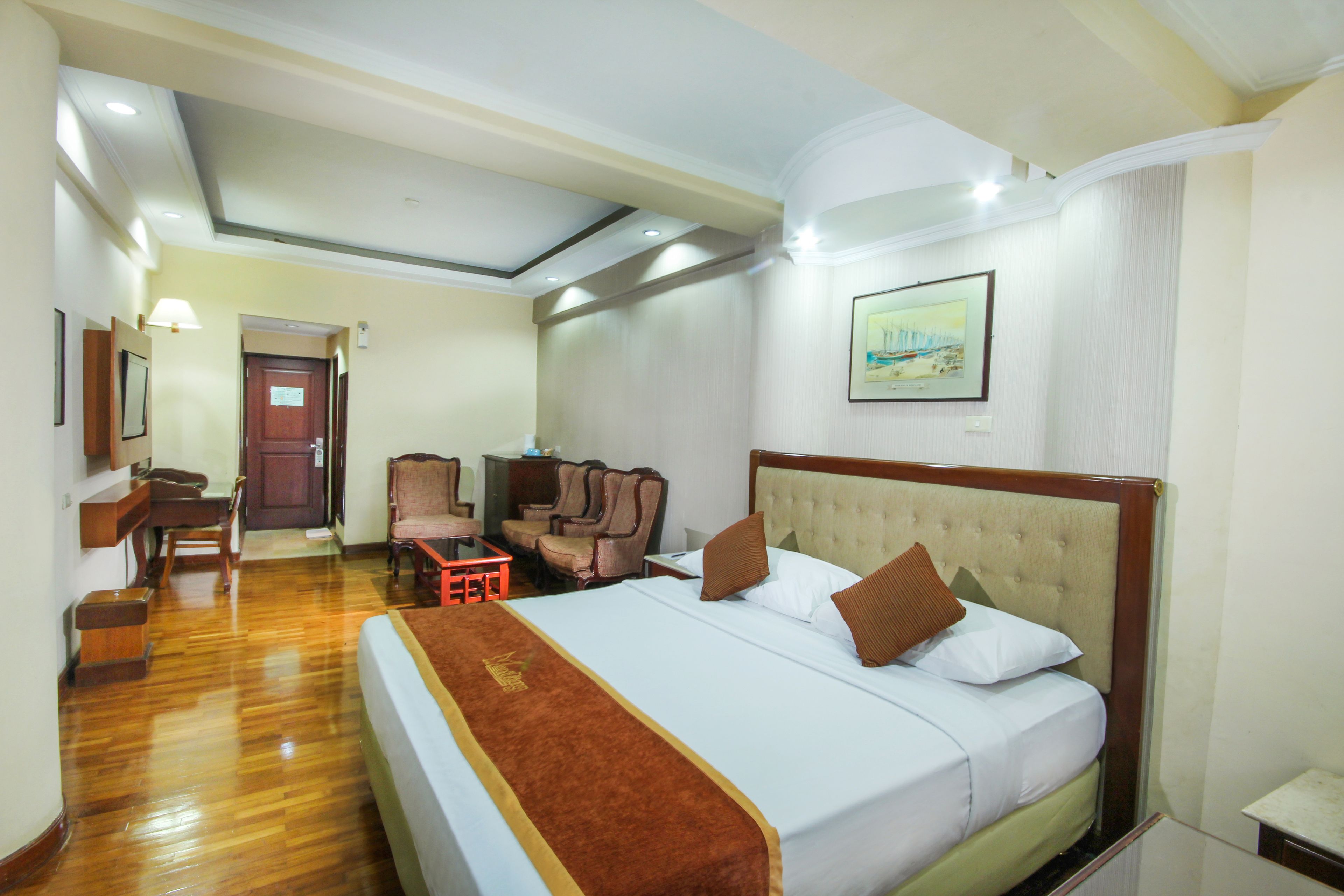 Une chambre d’hôtel avec un grand lit, un bureau, deux chaises, une petite table et une porte.