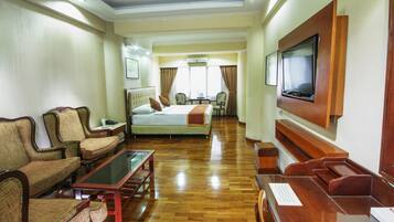 Habitación de hotel con cama, dos sillones, un sofá, televisor y escritorio con silla.