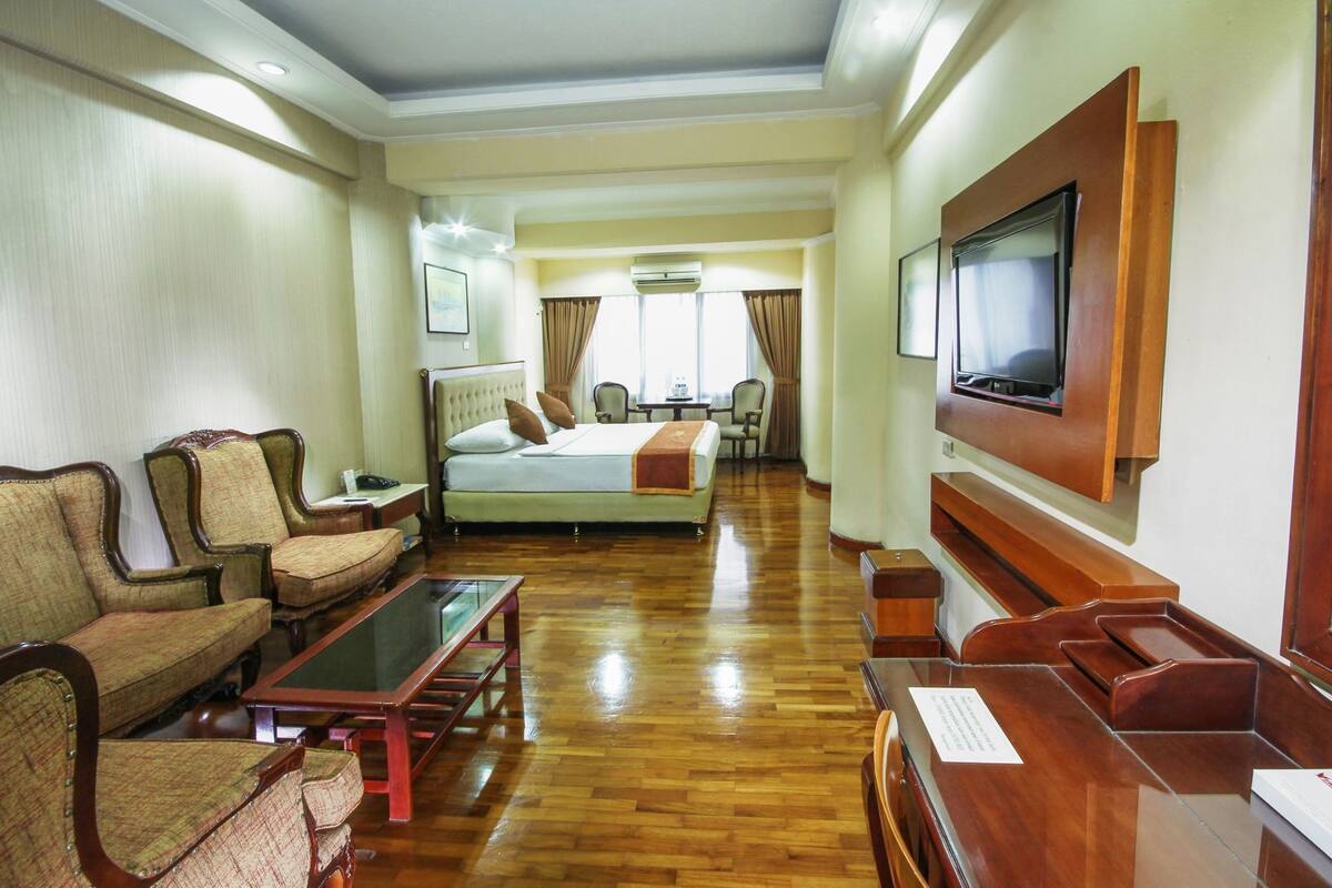 A hotel room with a bed, two armchairs, a coffee table, a TV, and a desk with a chair.