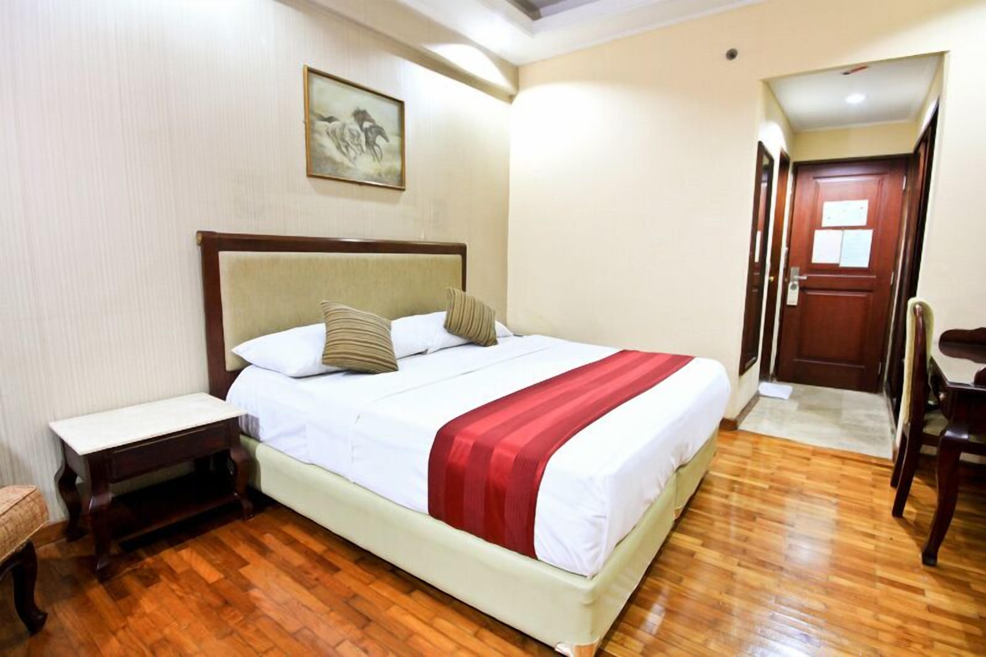 Een hotelkamer met een bed, nachtkastje, stoel en een deur.