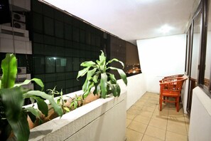 A balcony with potted plants, a wooden chair, and a view of the city at night. - Grand Menteng Hotel (Jakarta)