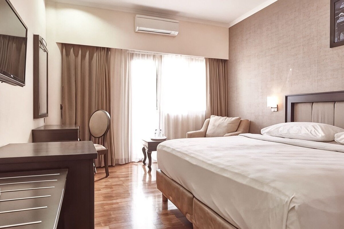 Una habitación de hotel con cama, escritorio, silla, mesita y espejo.