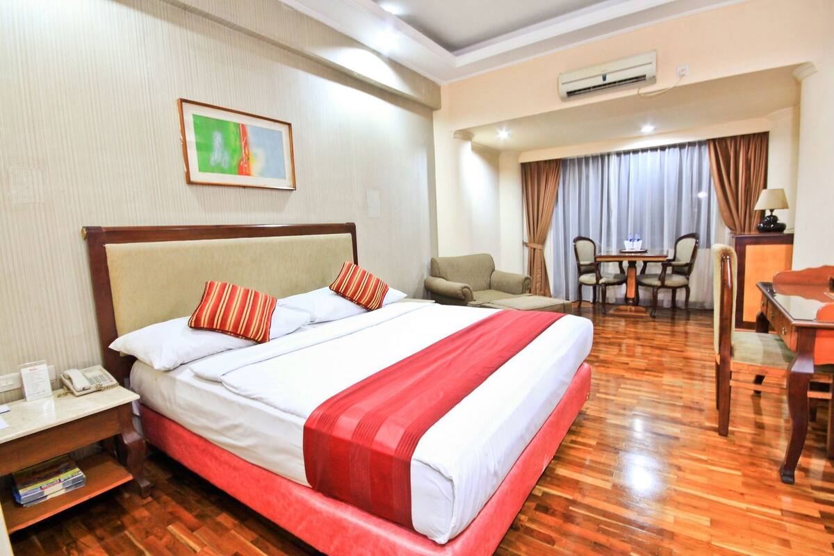 A hotel room with a large bed, a desk, a chair, and a dining table.