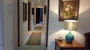 A hallway with a patterned rug, a wooden table with a lamp, and a framed painting on the wall. - Magaliqua Guest House (Krugersdorp)