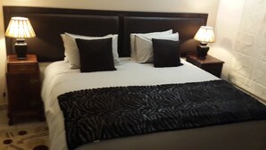 A neatly made bed with a black throw blanket, two bedside lamps, and a dark headboard. - Magaliqua Guest House (Krugersdorp)
