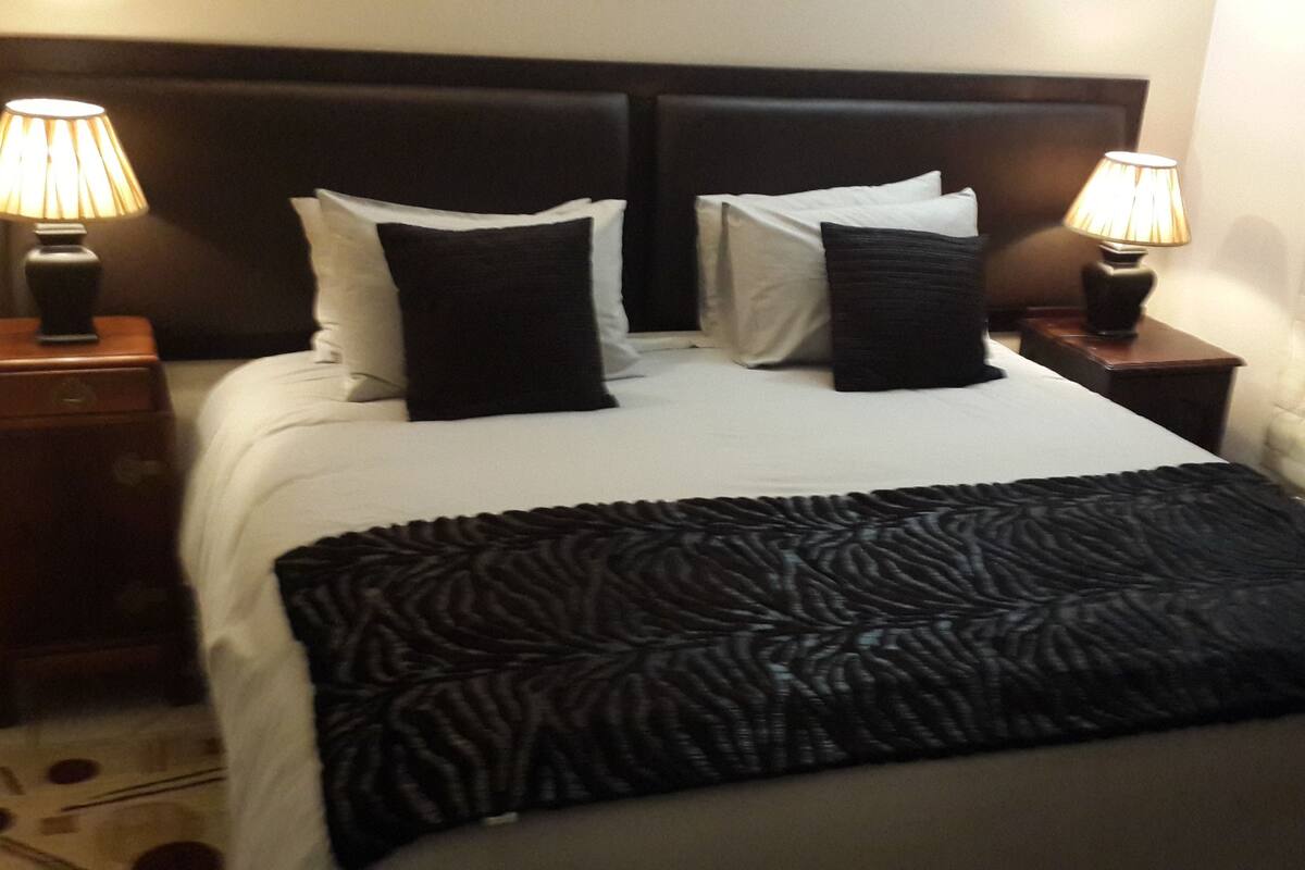 A neatly made bed with a black throw blanket, two bedside lamps, and a dark headboard.