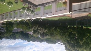 A building with a reflective water surface below, a balcony with hanging lights, and a fenced area with greenery. - Magaliqua Guest House (Krugersdorp)