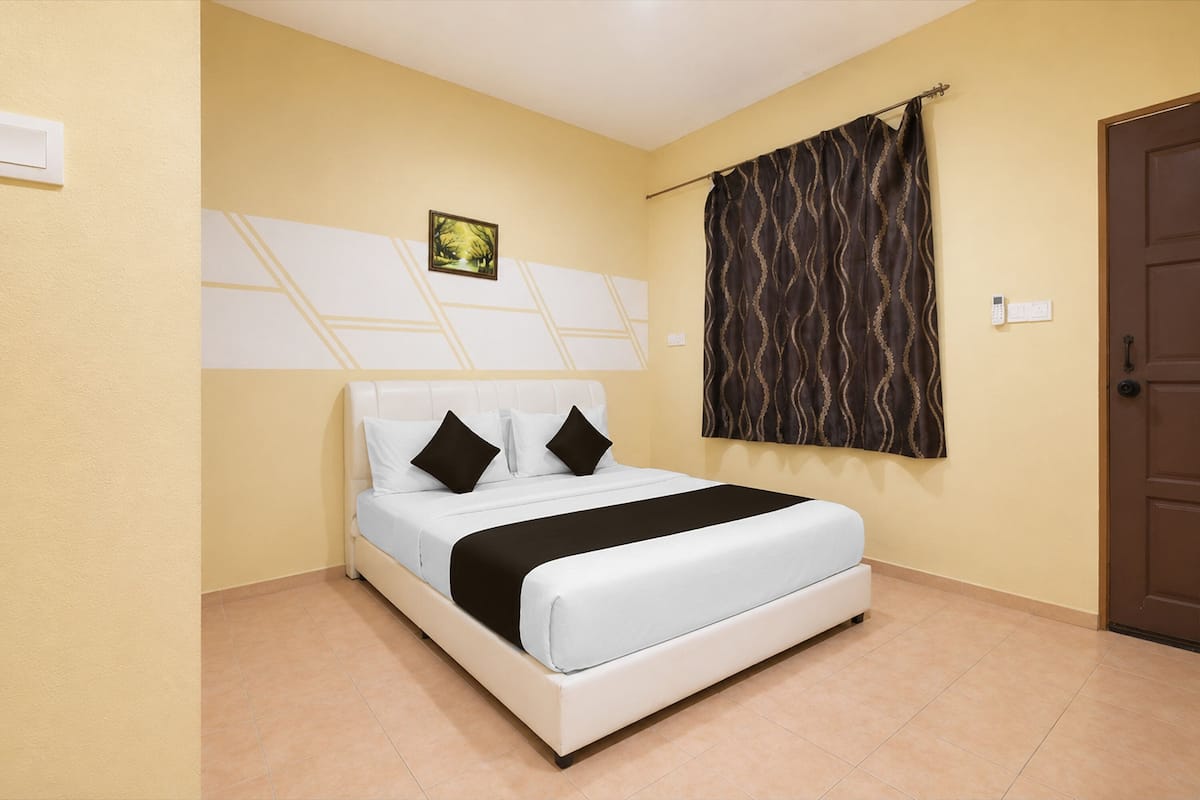 A bed with white bedding and black pillows, a wall-mounted picture, a patterned curtain, and a door.