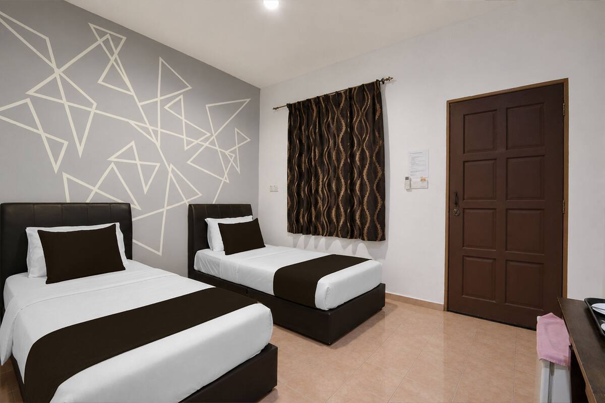 A hotel room with two beds, a patterned curtain, a brown door, and a geometric wall design.