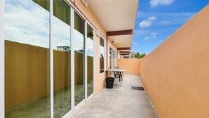 A covered outdoor area with a table and chairs, a trash bin, and a glass door leading to a balcony. - Collection O Langkawi Near Pantai Cenang formerly Tokman Inn (Langkawi)