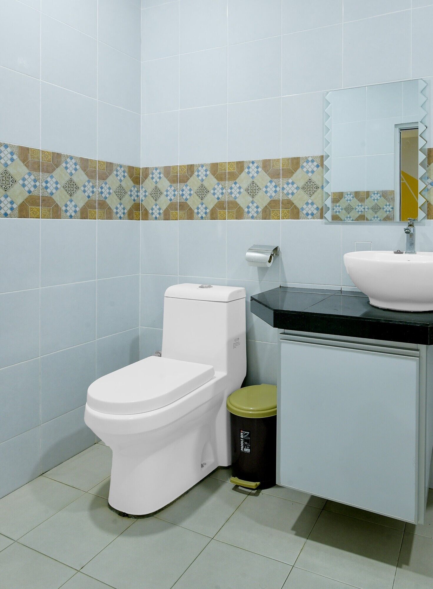 A bathroom with a toilet, sink, mirror, and patterned tiles.