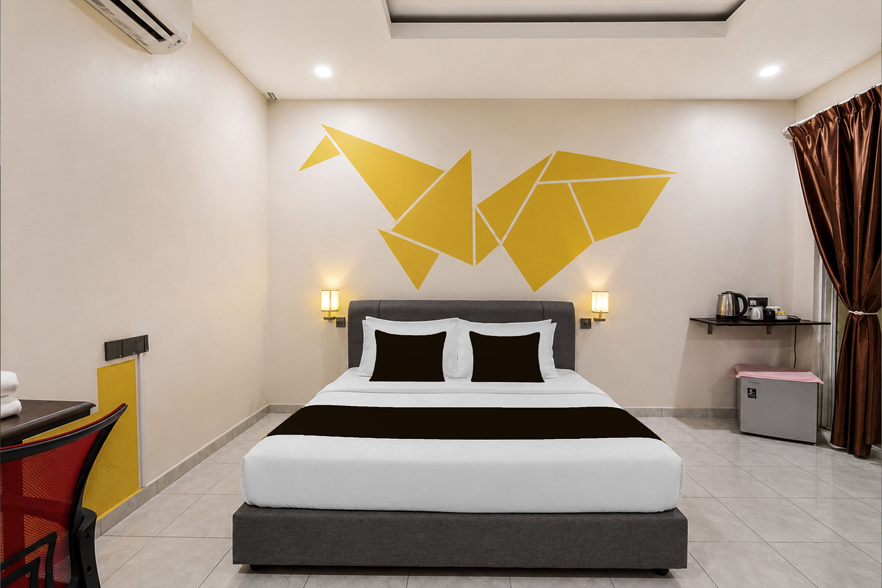 A modern hotel room with a large bed, a desk with a chair, a small kitchenette, and a decorative wall piece.