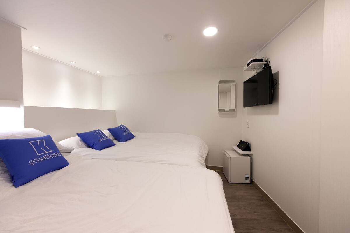 Une chambre d’hôtel avec deux lits, du linge de lit blanc et des oreillers bleus ornés d’un logo.