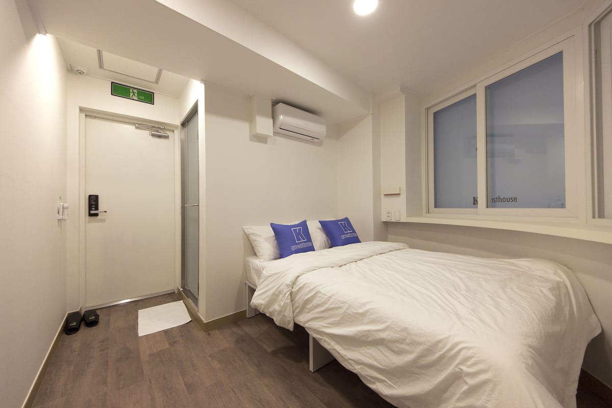 Une chambre d’hôtel équipée d’un lit, d’une fenêtre, d’un appareil de climatisation et d’une porte avec un panneau indiquant la sortie de secours.