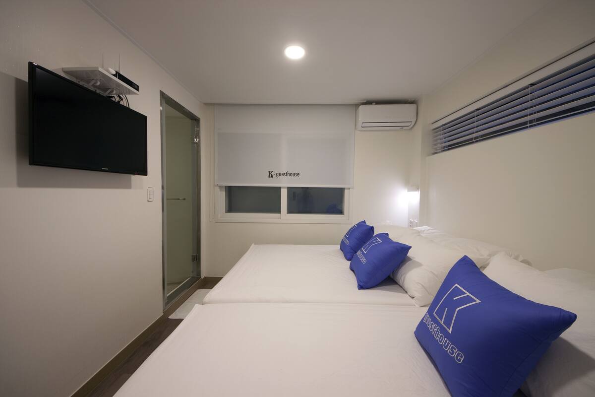 Une chambre d’hôtel avec un lit, un téléviseur à écran plat fixé au mur et une fenêtre avec des stores.