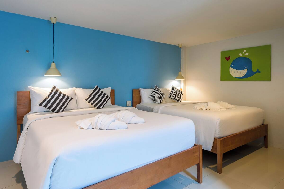 A hotel room with two beds, each with white bedding and striped pillows. There are two bedside lamps, and a wall painting of a whale.