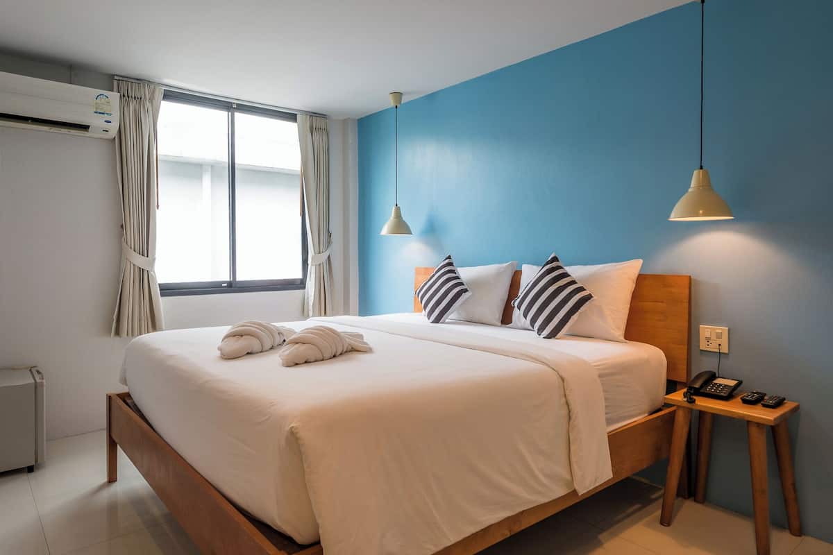 A hotel room with a bed, bedside table with a phone, and a window with curtains.