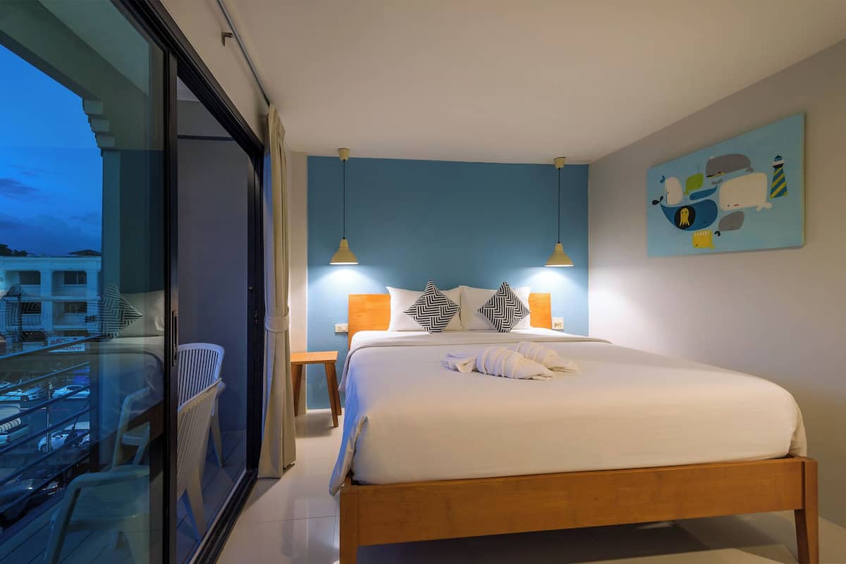 A modern hotel room with a large bed, two bedside lamps, a view balcony, and a nautical-themed wall art.