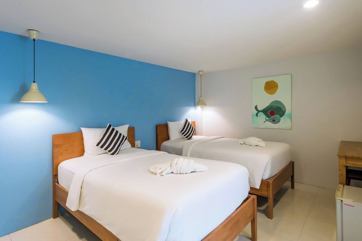 A hotel room with two beds, each with white bedding and striped pillows, a wooden headboard, and a painting on the wall.