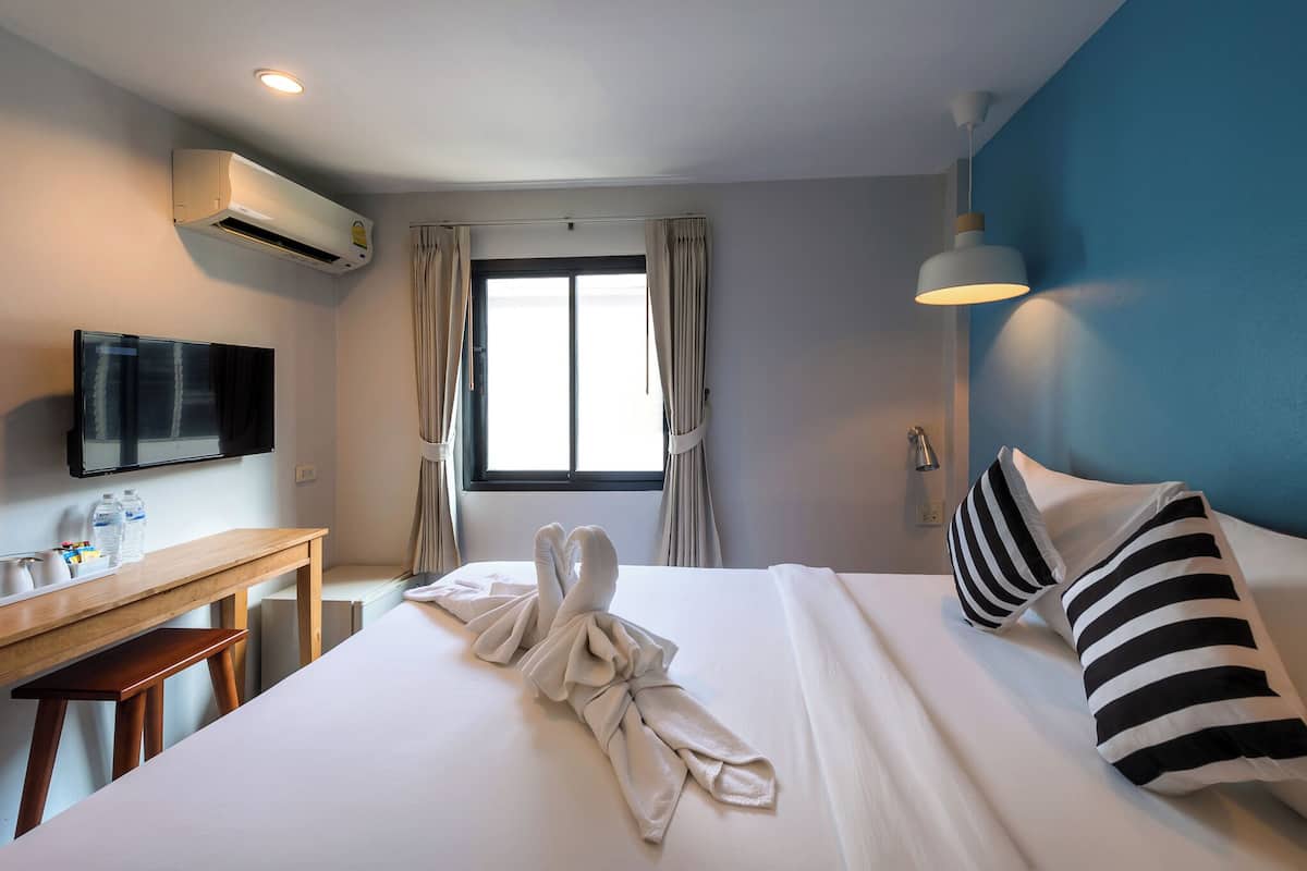 A hotel room with a bed, a desk, a TV, and an air conditioning unit.