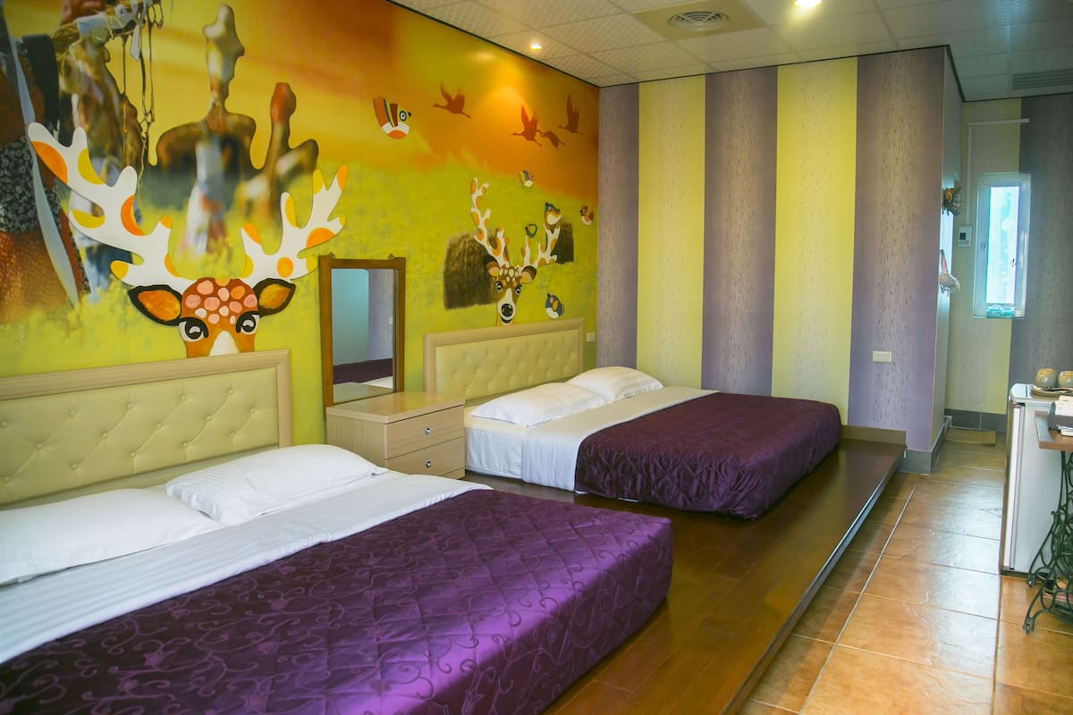 Habitación de hotel con dos camas, un espejo grande y un mural con ciervos y pájaros en la pared.