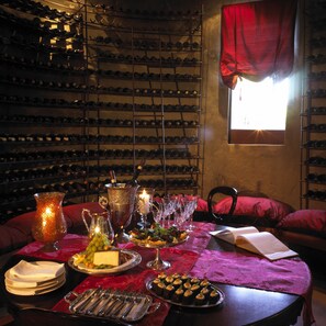 A wine cellar with racks of wine bottles, a table set for a meal with a candle, and a window with red curtains. - Tintswalo Safari (Bushbuckridge)