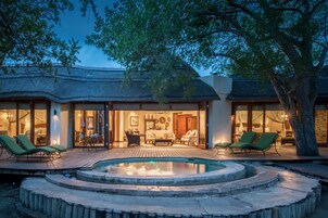 Una villa lujosa con piscina, mobiliario de exterior e interiores bien iluminados.