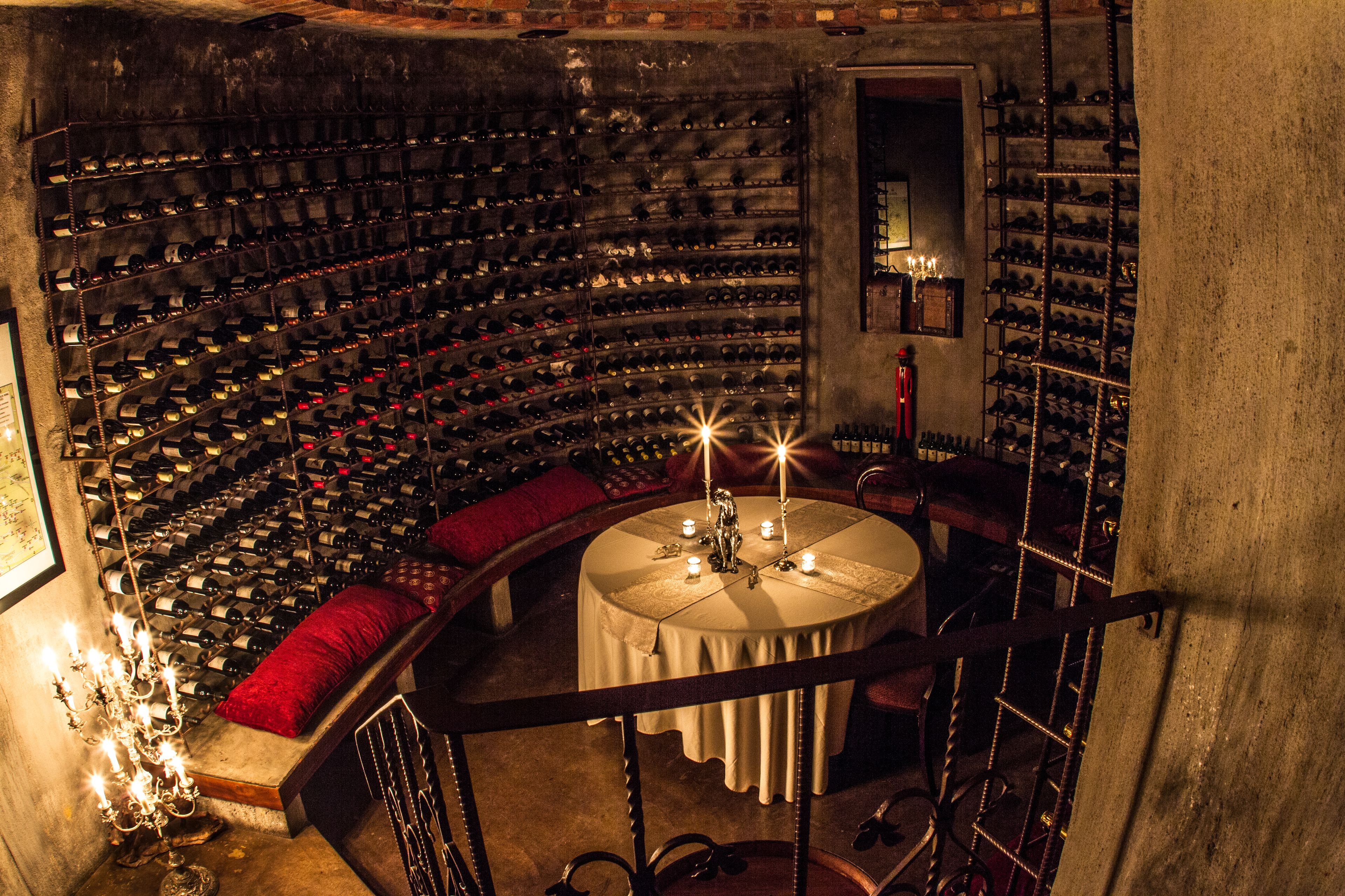 A wine cellar with multiple wine racks, a round table with candles, and red cushioned seating.
