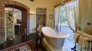 Un baño espacioso con una bañera independiente, un muro de acento de piedra y vistas al exterior a través de amplias ventanas.