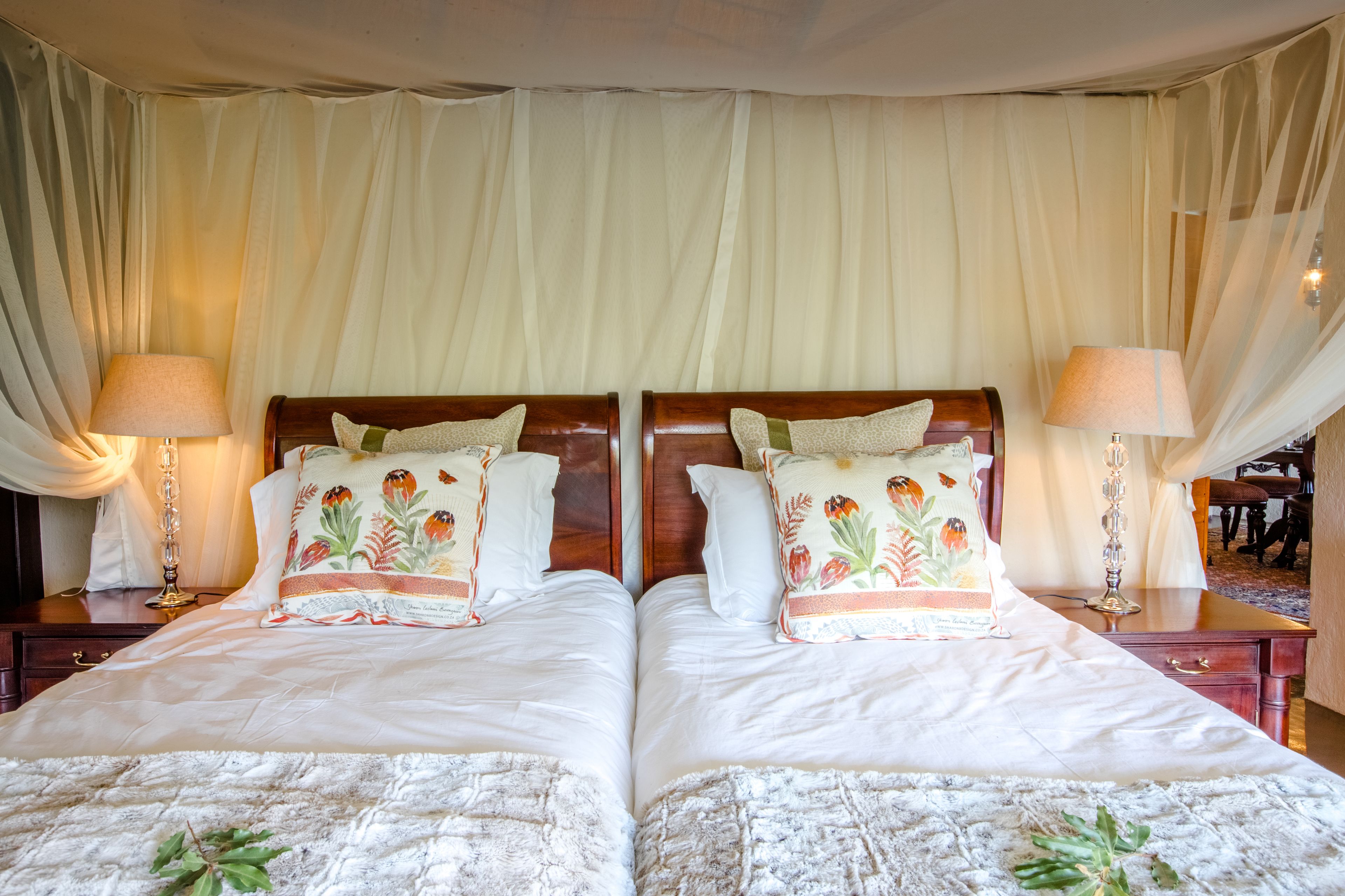 A double bed with floral pillows, a wooden headboard, and a white bedspread. There are two bedside tables with lamps and a decorative mirror.