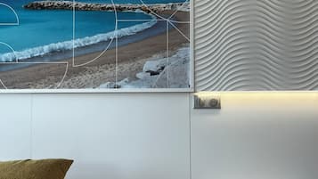 Ein Schlafzimmer mit einem Bett, einem Nachttisch, einem an der Wand befestigten Bild von einem Strand und einer strukturierten Wandverkleidung.