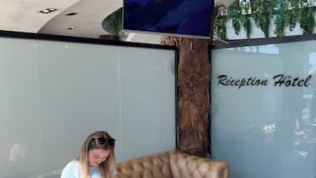 A woman sitting on a brown leather sofa reading a magazine.