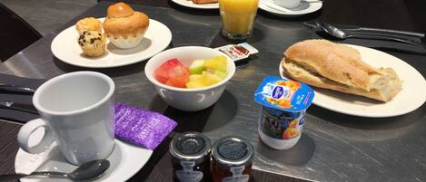 A breakfast table with croissants, muffins, fruit, juice, yogurt, jam, and a baguette.