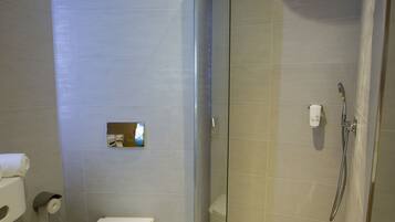A modern bathroom with a glass-enclosed shower, a toilet, and a hand dryer.