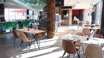 En modern restaurang med en central träkolonn, glasräcken och en trappa. Bord och stolar är placerade för att skapa en trevlig matplats.