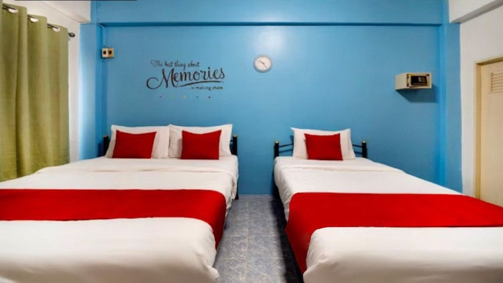 Habitación con dos camas, cada una con ropa de cama roja y blanca, y una pared azul con un reloj y un cartel que dice 'The best things about Memories are making them'.
