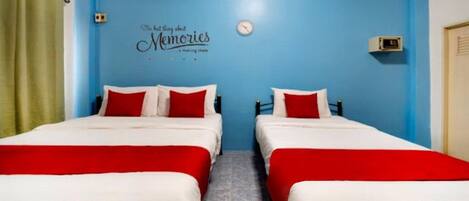 Habitación con dos camas, cada una con ropa de cama roja y blanca, y una pared azul con un reloj y un cartel que dice 'The best things about Memories are making them'.